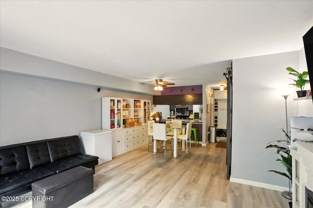 living area featuring light wood-style flooring, ceiling fan, and baseboards