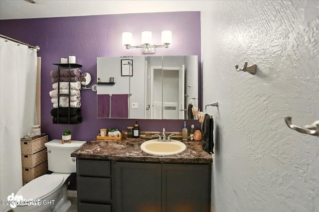 full bathroom with a textured wall, toilet, vanity, and curtained shower