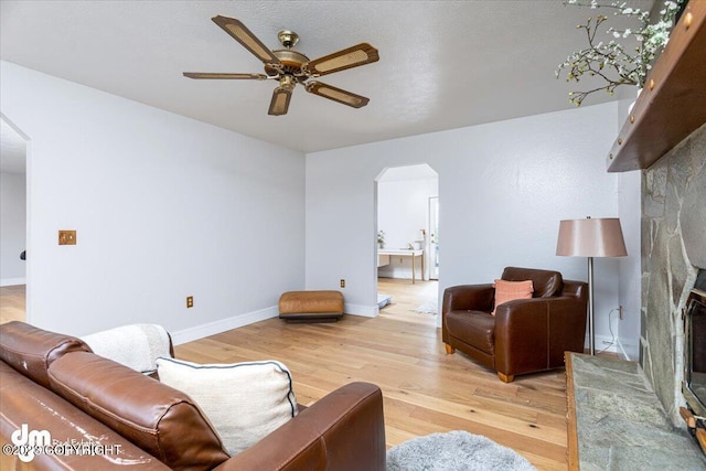 174 E Leota St, Wasilla, AK 99654 - living room featuring arched walkways, a ceiling fan, light wood-type flooring, baseboards, and a stone fireplace