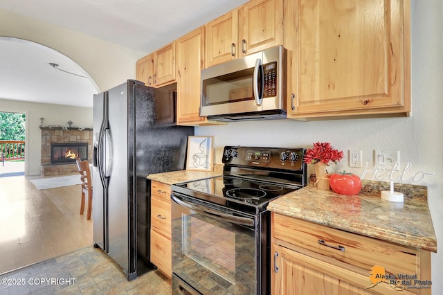 4147 Hampton Dr # 10D, Anchorage, AK 99504 - kitchen with black appliances, light brown cabinets, a fireplace, arched walkways, and light stone countertops