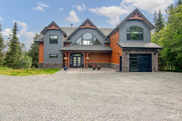 52619 Chumelina Ct, Kasilof, AK 99610 - view of front facade with french doors, gravel driveway, an attached garage, stone siding, and roof with shingles