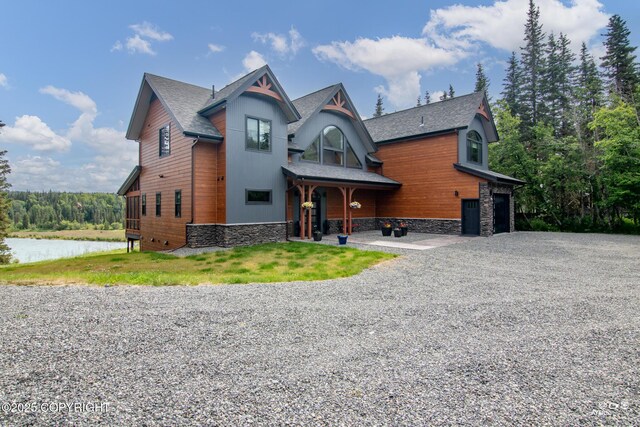 52619 Chumelina Ct, Kasilof, AK 99610 - view of front of house featuring gravel driveway, a water view, stone siding, a shingled roof, and an attached garage