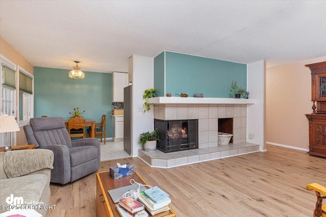 1920 E 56th Ave, Anchorage, AK 99507 - living room with wood finished floors, a tiled fireplace, a textured ceiling, baseboards, and a chandelier