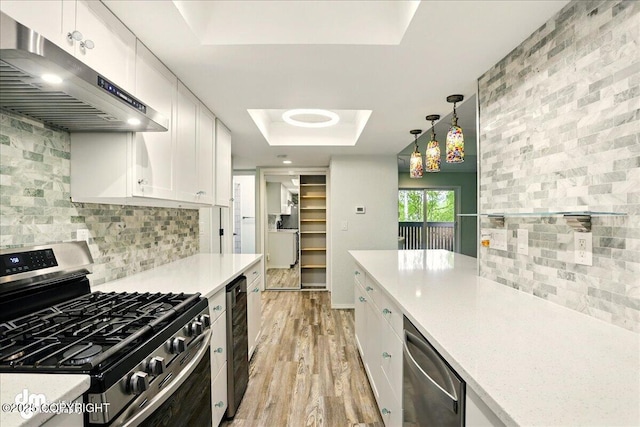 7341 Huntsmen Cir Unit 19C, Anchorage, AK 99518 - kitchen with appliances with stainless steel finishes, under cabinet range hood, a tray ceiling, wine cooler, and white cabinetry