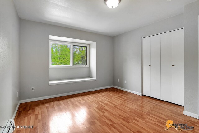 18739 Sarichef Loop, Eagle River, AK 99577 - unfurnished bedroom featuring a baseboard heating unit, light wood-style flooring, baseboards, and a closet