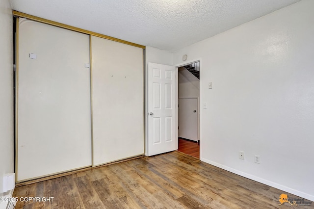 7075 Weimer Rd # 6, Anchorage, AK 99502 - unfurnished bedroom featuring wood finished floors, a closet, a textured ceiling, and baseboards
