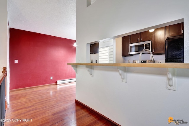 7075 Weimer Rd # 6, Anchorage, AK 99502 - kitchen featuring stainless steel microwave, freestanding refrigerator, baseboard heating, light wood finished floors, and a breakfast bar area