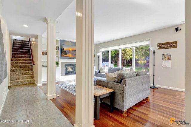 740 Botanical Heights Cir, Anchorage, AK 99515 - living room featuring ornate columns, stairs, baseboards, a glass covered fireplace, and wood finished floors