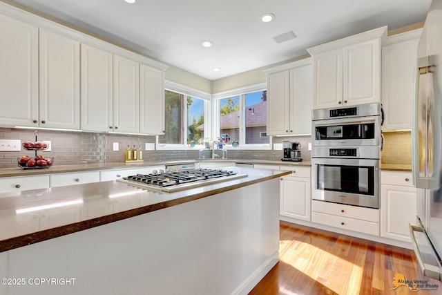 740 Botanical Heights Cir, Anchorage, AK 99515 - kitchen with stainless steel appliances, white cabinets, a sink, light wood-style flooring, and tasteful backsplash
