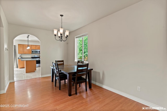 1675 E Pintail Dr, Wasilla, AK 99645 - dining area featuring a chandelier, arched walkways, light wood-type flooring, and baseboards
