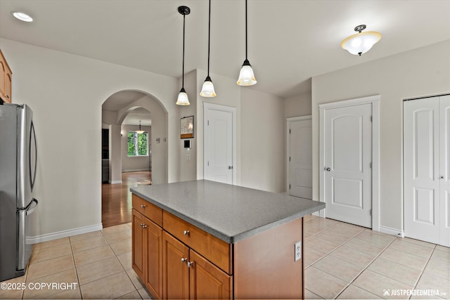 1675 E Pintail Dr, Wasilla, AK 99645 - kitchen with freestanding refrigerator, light tile patterned flooring, arched walkways, a center island, and brown cabinetry