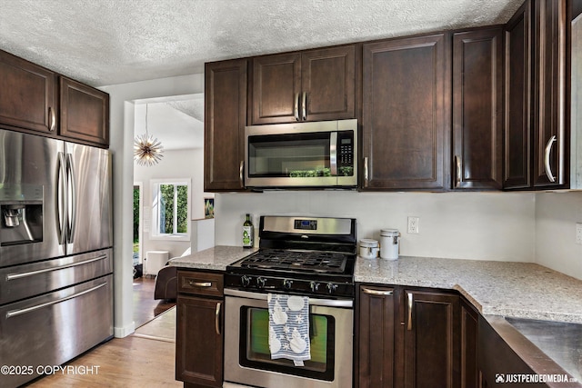 1551 S Oat St, Wasilla, AK 99654 - kitchen with stainless steel appliances, dark brown cabinetry, light wood finished floors, light stone countertops, and a textured ceiling