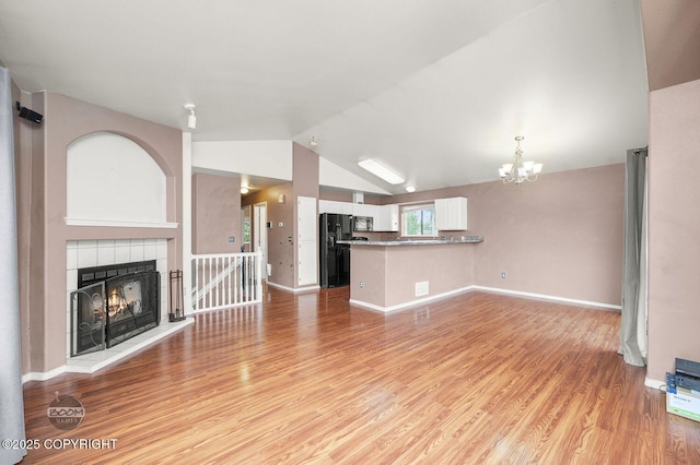 3933 Sycamore Loop, Anchorage, AK 99504 - unfurnished living room with a chandelier, light wood-style flooring, vaulted ceiling, a tile fireplace, and baseboards