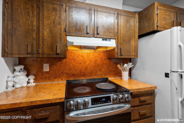 4433 San Ernesto Ave # 104, Anchorage, AK 99508 - kitchen featuring under cabinet range hood, stainless steel range with electric stovetop, freestanding refrigerator, backsplash, and light countertops