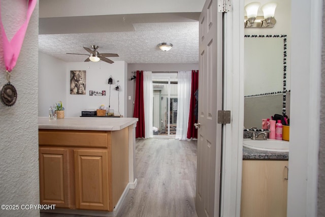 1701 Russian Jack Dr # D3, Anchorage, AK 99508 - kitchen with a sink, ceiling fan, light wood-style flooring, a textured ceiling, and a peninsula