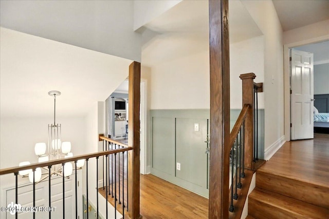 12900 Wellsford Cir, Anchorage, AK 99516 - hall featuring wood finished floors, a chandelier, an upstairs landing, and a wainscoted wall