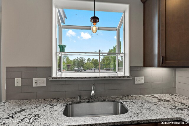 1506 M St, Anchorage, AK 99501 - kitchen featuring a sink, decorative backsplash, dark brown cabinets, light stone countertops, and hanging light fixtures