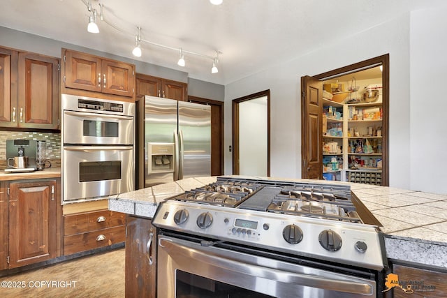 15245 Longbow Dr, Anchorage, AK 99516 - kitchen featuring appliances with stainless steel finishes, brown cabinets, tile countertops, and decorative backsplash