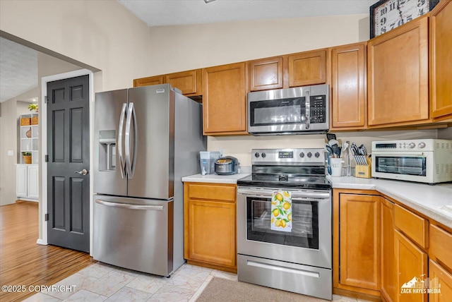 19705 Citation Rd, Eagle River, AK 99577 - kitchen featuring appliances with stainless steel finishes, light countertops, brown cabinetry, light marble finish flooring, and lofted ceiling