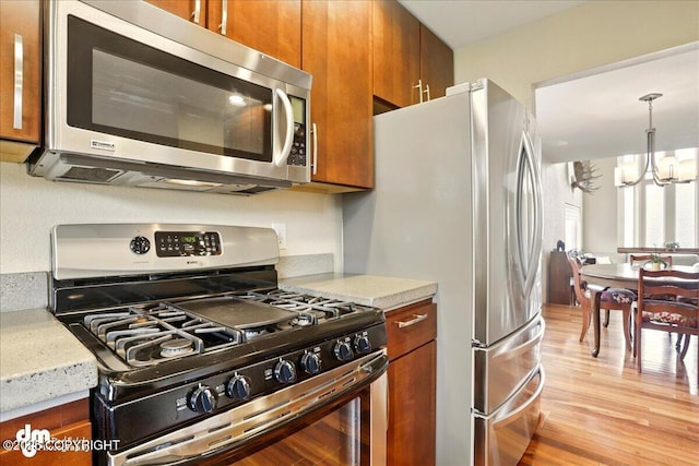 10410 Constitution St, Anchorage, AK 99515 - kitchen featuring stainless steel appliances, brown cabinets, a chandelier, light wood-style flooring, and light stone counters