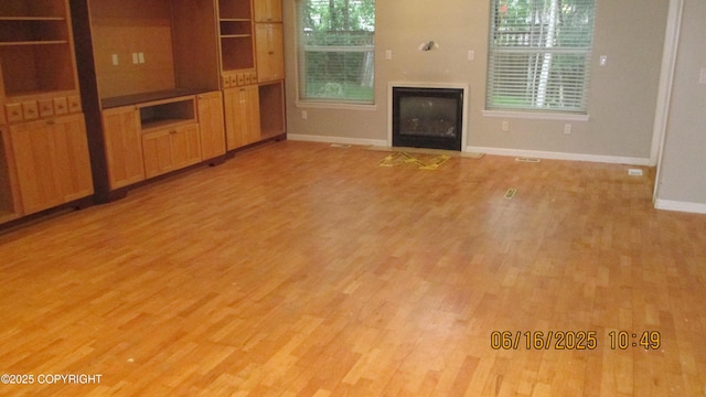 2024 Oxbow Cir, Anchorage, AK 99516 - unfurnished living room featuring light wood-style flooring, healthy amount of natural light, and a glass covered fireplace