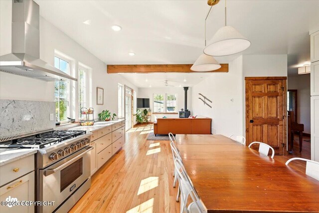 7350 E Narnia Cir, Palmer, AK 99645 - kitchen featuring wall chimney exhaust hood, high end stainless steel range oven, light wood-style floors, beamed ceiling, and plenty of natural light