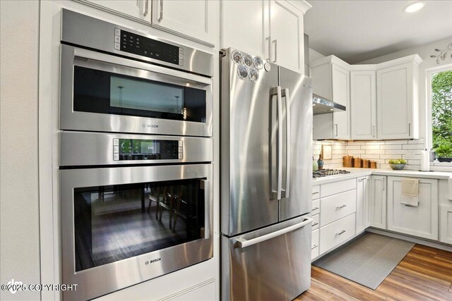 8727 Turlock Dr, Eagle River, AK 99577 - kitchen with stainless steel appliances, wood finished floors, light countertops, white cabinetry, and backsplash