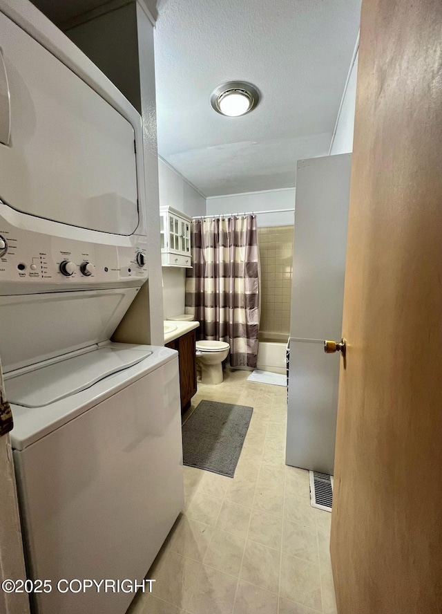 10250 Jamestown Dr # B-09, Anchorage, AK 99507 - bathroom featuring stacked washer / dryer, toilet, shower / bath combo with shower curtain, vanity, and tile patterned flooring