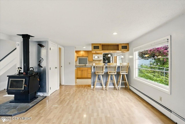 2527 Cottonwood St, Anchorage, AK 99508 - kitchen with a baseboard radiator, light wood finished floors, a wood stove, white microwave, and decorative backsplash