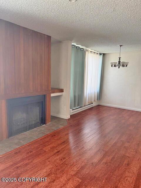 1008 Wildrose Ct, Anchorage, AK 99518 - unfurnished living room featuring a textured ceiling, a chandelier, a fireplace with flush hearth, wood finished floors, and a baseboard radiator