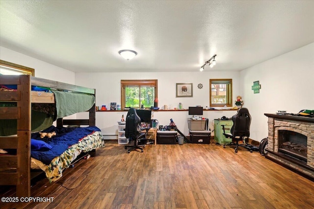 7965 S Settlers Bay Dr, Wasilla, AK 99623 - bedroom with wood-type flooring, a fireplace, a baseboard heating unit, a textured ceiling, and an office area
