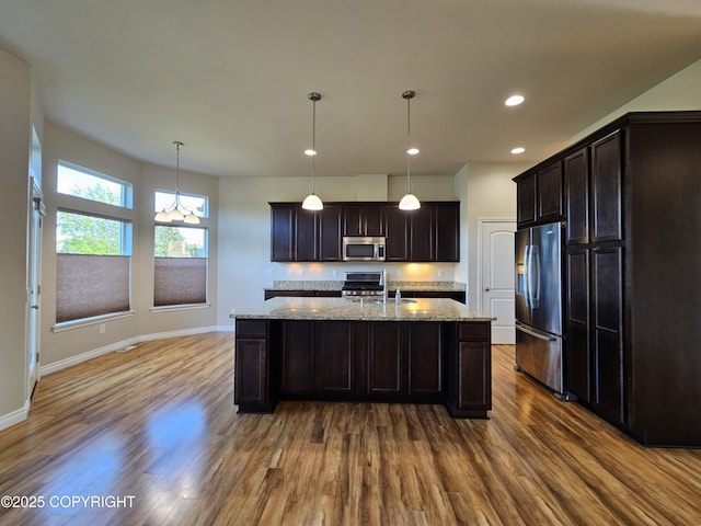 5523 Grand Teton Loop, Anchorage, AK 99502 - kitchen featuring stainless steel appliances, dark wood-type flooring, light stone counters, a center island with sink, and dark brown cabinetry