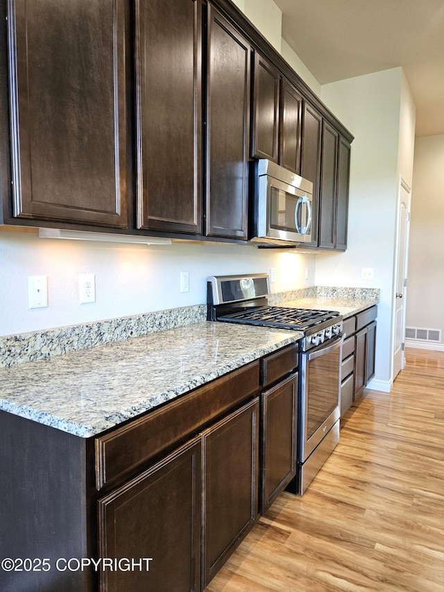 5523 Grand Teton Loop, Anchorage, AK 99502 - kitchen featuring appliances with stainless steel finishes, light wood-type flooring, light stone countertops, and dark brown cabinets