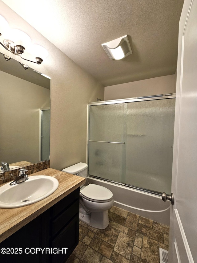 5523 Grand Teton Loop, Anchorage, AK 99502 - bathroom featuring vanity, stone finish floors, toilet, combined bath / shower with glass door, and a textured ceiling