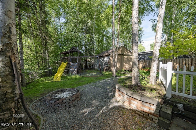 13311 Cove Cir, Anchorage, AK 99515 - fenced backyard featuring a playground, a fire pit, and a storage shed