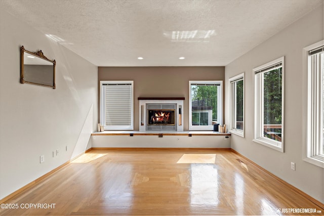18704 Snowy Plover Cir, Anchorage, AK 99516 - unfurnished living room with a warm lit fireplace, a textured ceiling, baseboards, wood finished floors, and recessed lighting
