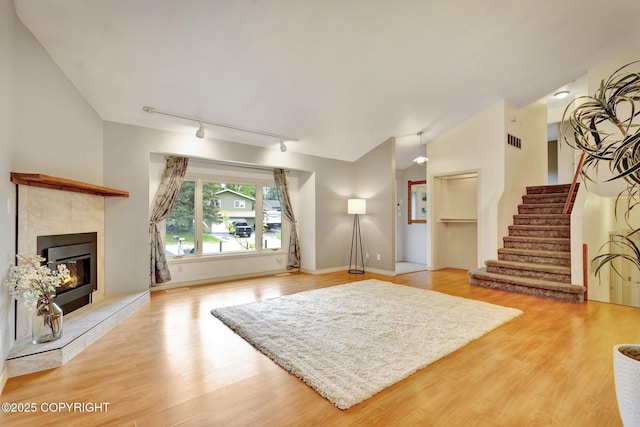 13521 Ebbtide Cir, Anchorage, AK 99516 - unfurnished living room featuring rail lighting, a tile fireplace, light wood-style flooring, stairs, and lofted ceiling