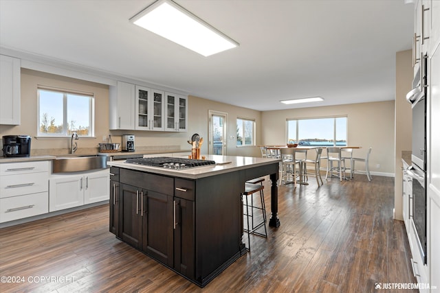 5322 S Big Lake Rd, Big Lake, AK 99652 - kitchen with stainless steel gas stovetop, white cabinetry, a breakfast bar area, glass insert cabinets, and dark wood finished floors