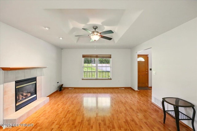22030 Birch Creek Dr, Chugiak, AK 99567 - unfurnished living room with a tray ceiling, light wood finished floors, a tile fireplace, a ceiling fan, and baseboards