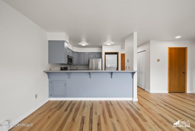 4109 Lynn Dr # 121, Anchorage, AK 99508 - kitchen featuring appliances with stainless steel finishes, stacked washing machine and dryer, gray cabinetry, a peninsula, and a kitchen bar