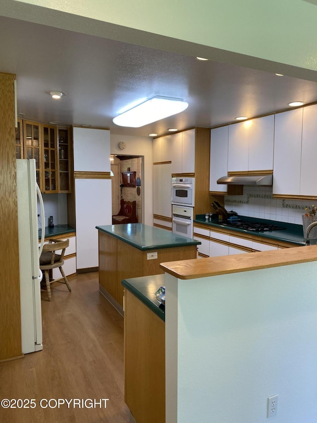 3316 Vassar Dr, Anchorage, AK 99508 - kitchen featuring white appliances, wood finished floors, dark countertops, a center island, and decorative backsplash