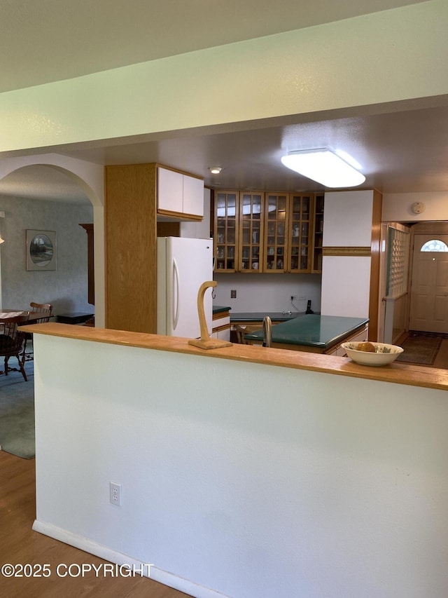3316 Vassar Dr, Anchorage, AK 99508 - kitchen with freestanding refrigerator, arched walkways, glass insert cabinets, wood finished floors, and white cabinetry