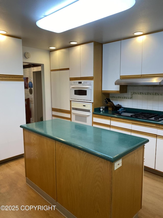 3316 Vassar Dr, Anchorage, AK 99508 - kitchen featuring light wood-type flooring, tasteful backsplash, dark countertops, under cabinet range hood, and a kitchen island