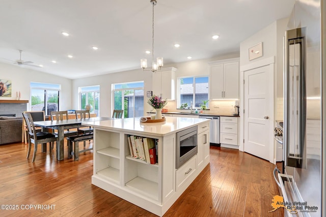 5466 Sandhill Loop, Anchorage, AK 99502 - kitchen featuring appliances with stainless steel finishes, white cabinetry, hanging light fixtures, a ceiling fan, and a fireplace