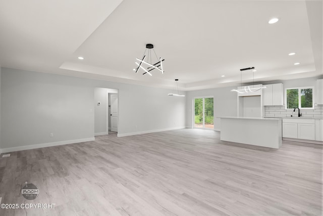 8328 S Ira Dr, Wasilla, AK 99623 - unfurnished living room featuring a raised ceiling, a chandelier, recessed lighting, light wood-type flooring, and plenty of natural light
