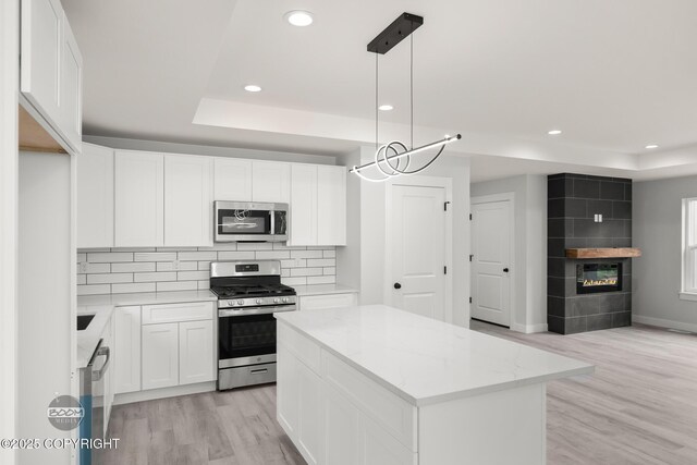 8328 S Ira Dr, Wasilla, AK 99623 - kitchen with stainless steel appliances, recessed lighting, light wood-style floors, a raised ceiling, and a fireplace