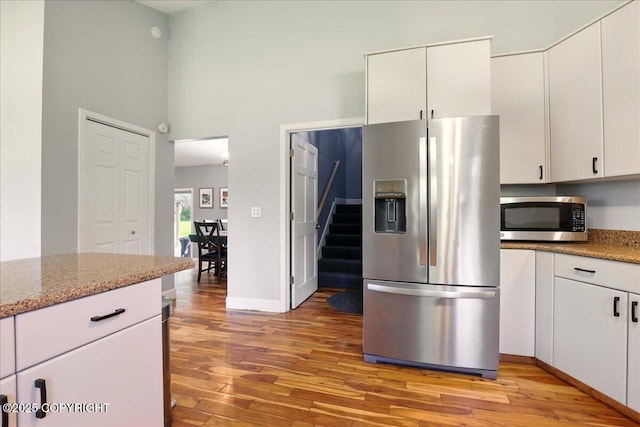 9701 Homestead Trl, Anchorage, AK 99507 - kitchen with stainless steel appliances, light wood-type flooring, a towering ceiling, white cabinets, and light stone countertops