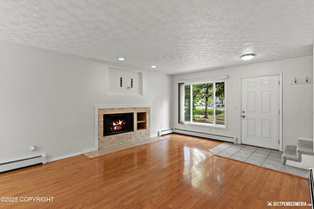11730 Nix Ct, Anchorage, AK 99515 - unfurnished living room featuring a baseboard heating unit, wood finished floors, a tile fireplace, a textured ceiling, and baseboards