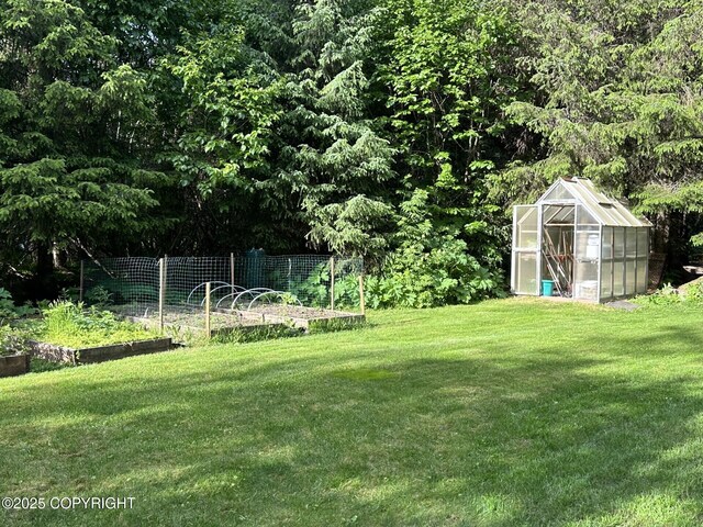 34008 Orlander Ave, Seward, AK 99664 - view of green lawn with a greenhouse, a vegetable garden, an outbuilding, and a wooded view
