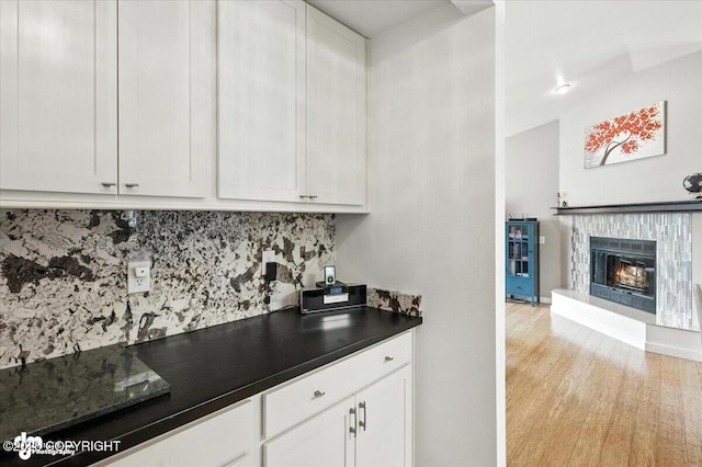 8968 Little Brook St, Anchorage, AK 99507 - kitchen with tasteful backsplash, dark countertops, white cabinets, a glass covered fireplace, and light wood-style flooring